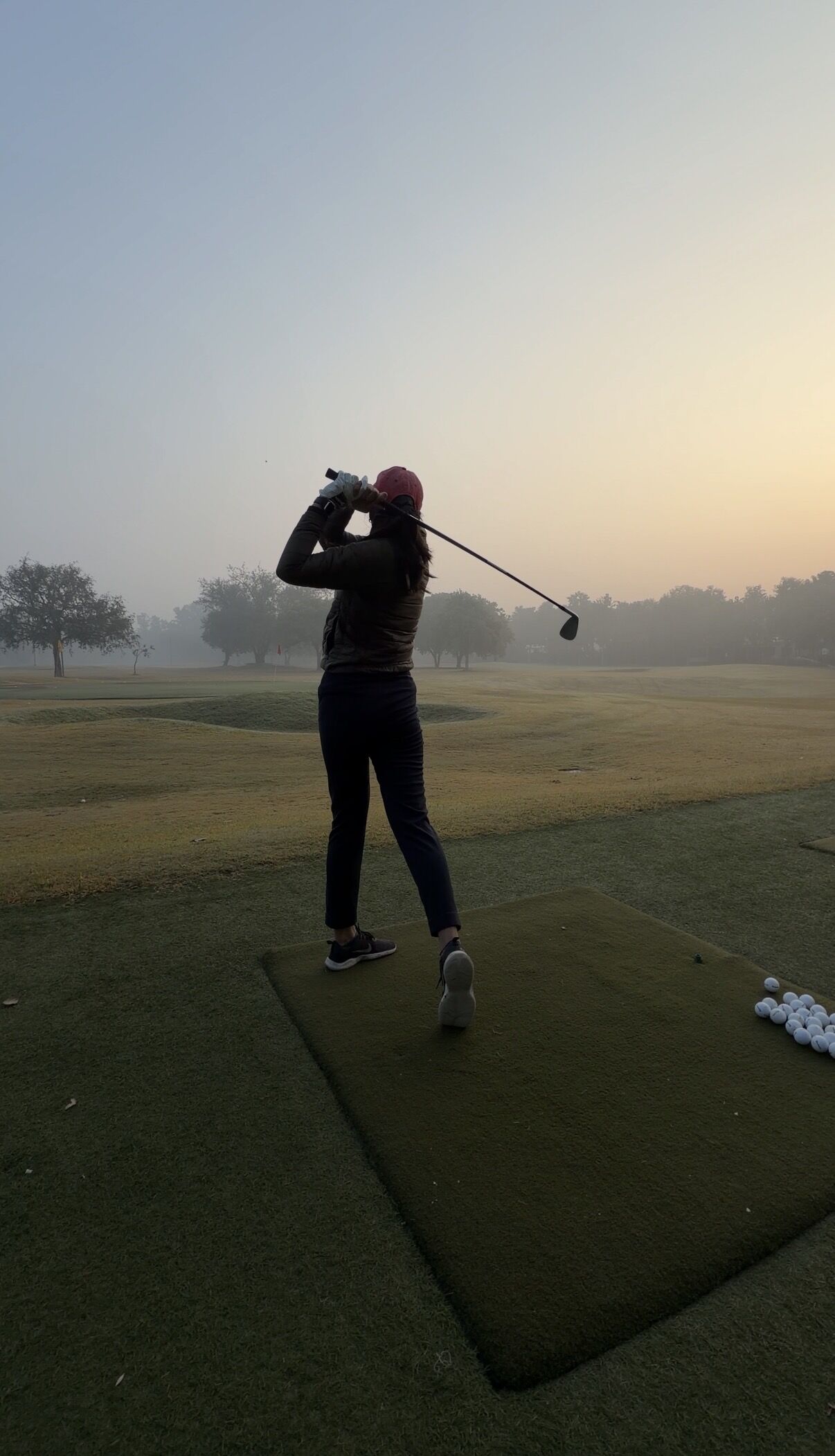 Soumya Goel practicing golf at sunrise on a driving range